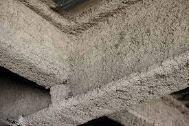 A corner of a building's ceiling that is covered in asbestos which looks a tannish white color and very bumpy. Reusing building material is prohibited for asbestos